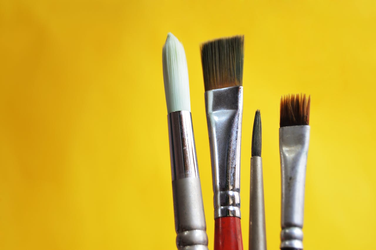 about-us Close-up of varied paint brushes against a bright yellow backdrop.