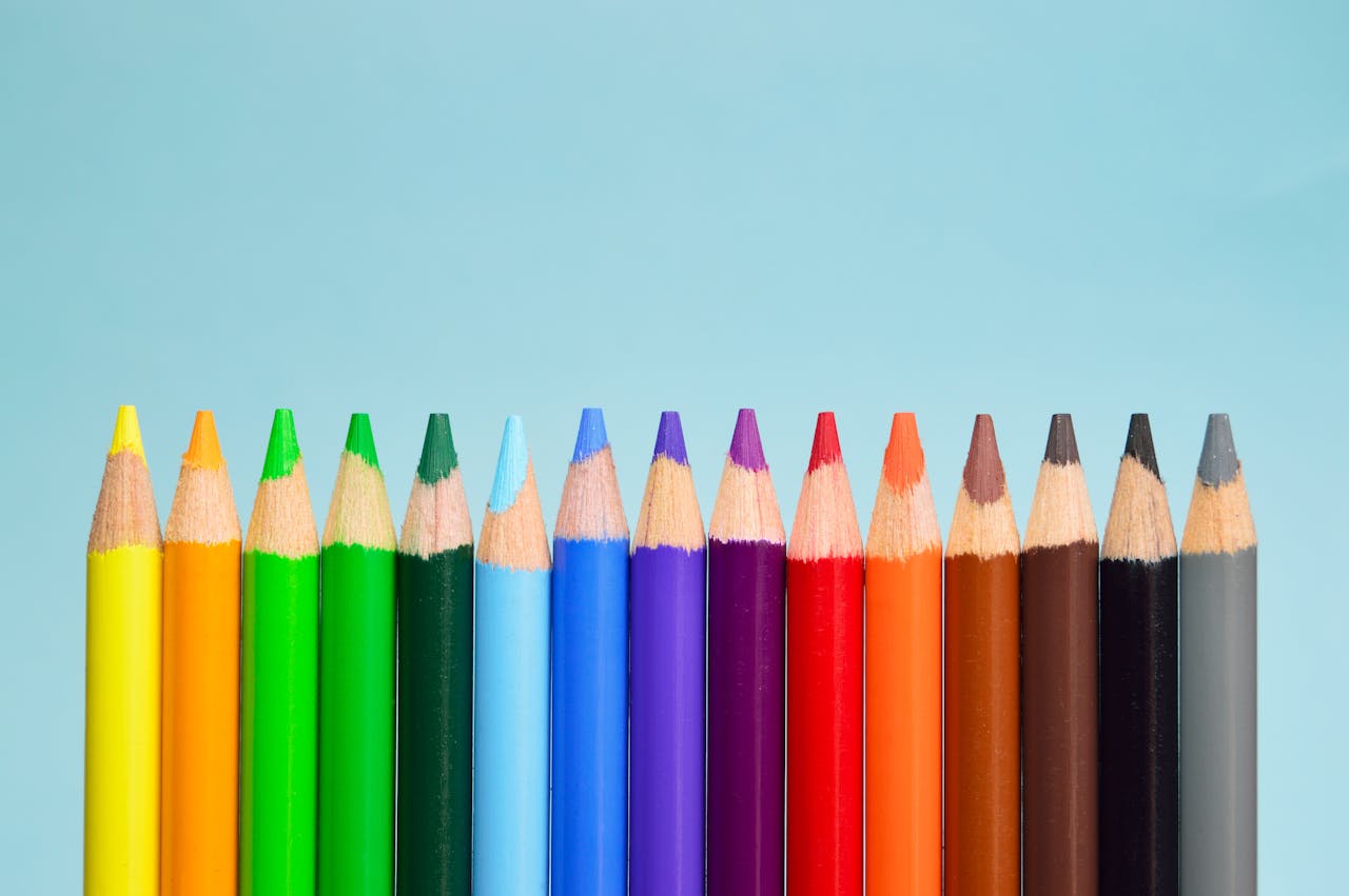 services-01 A row of vibrant colored pencils lined up on a soft blue background, showcasing a spectrum of colors.